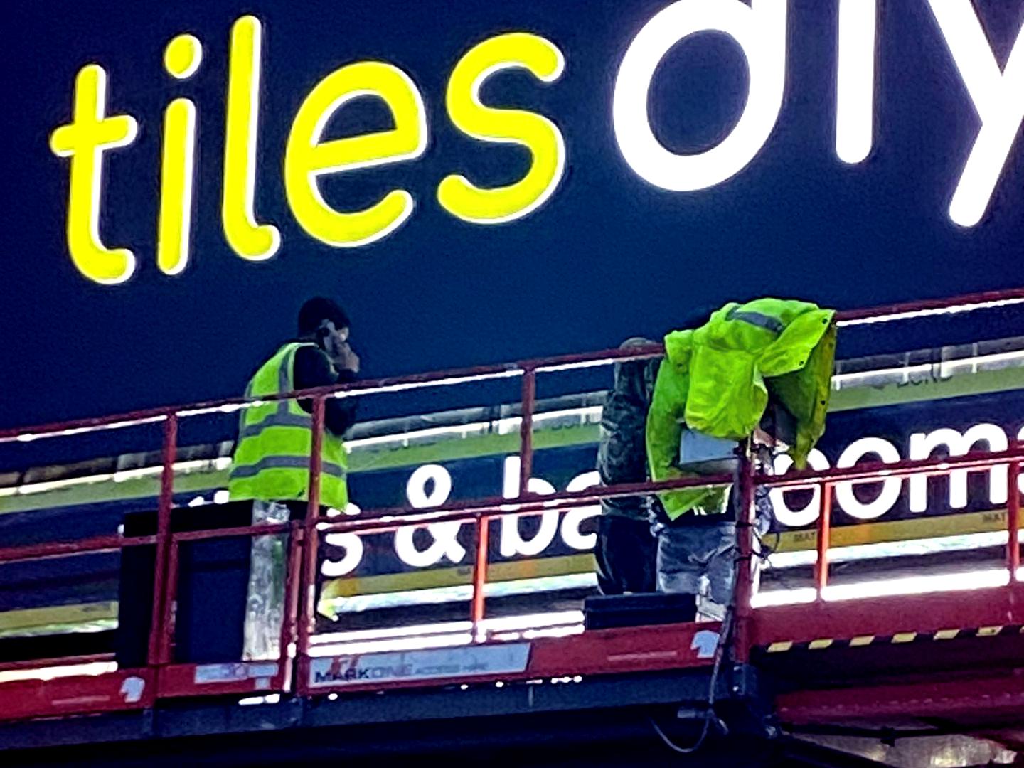 Workers installing the illuminated Tiles DIY signage on the storefront.